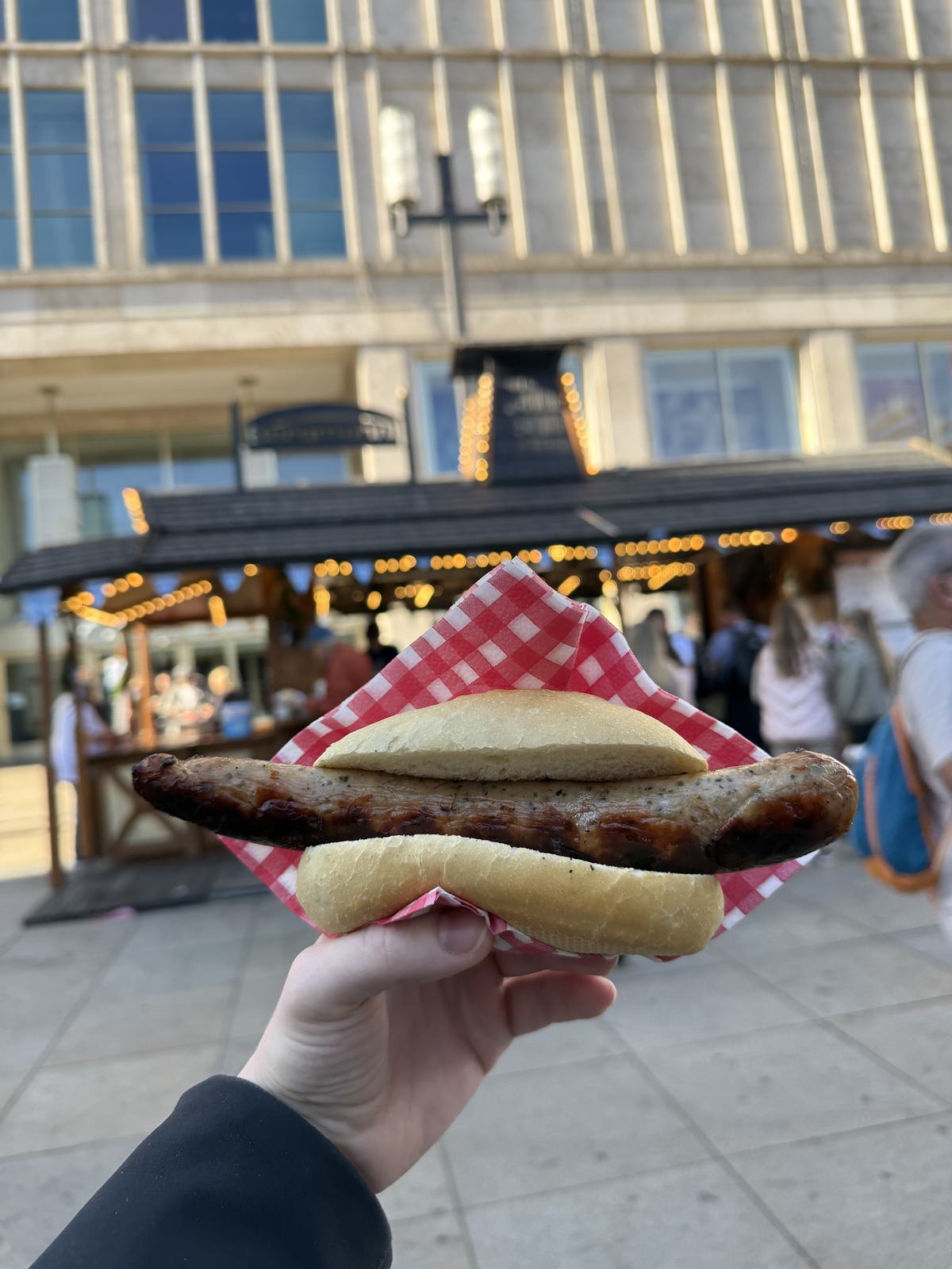A Bratwurst held up in front of the market stalls