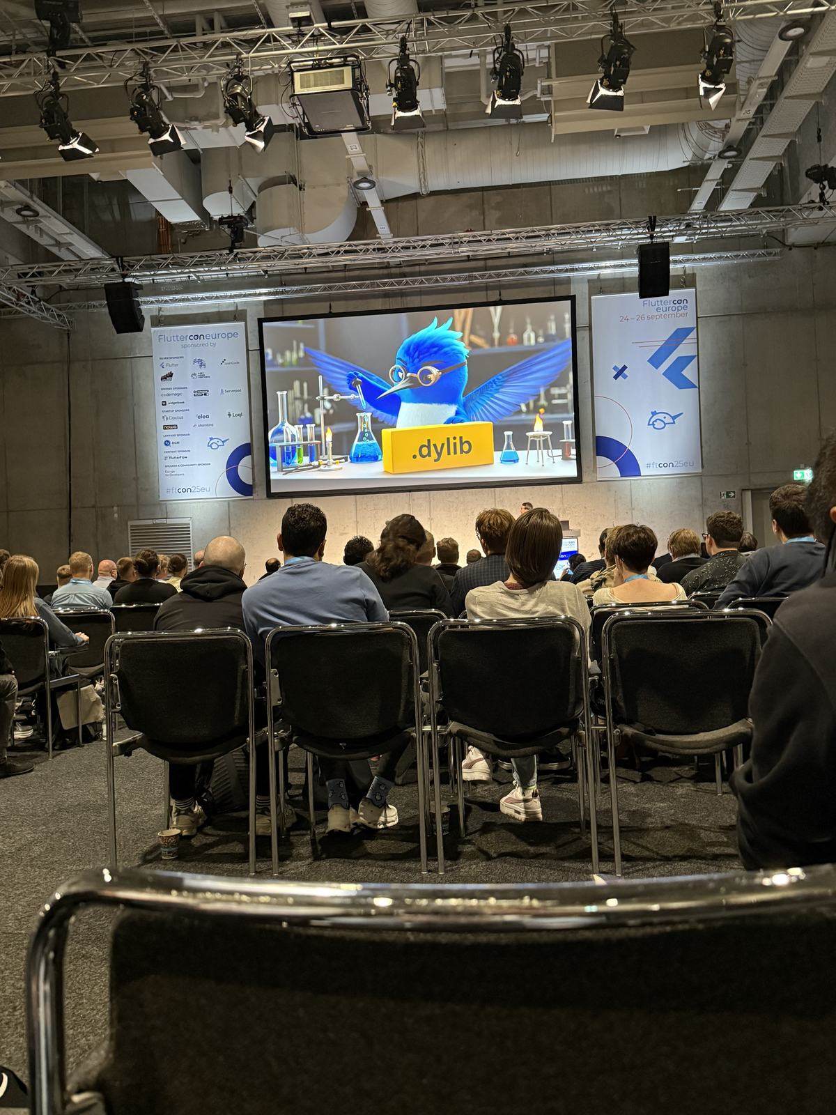 A full Fluttercon auditorium with Dash on the screen