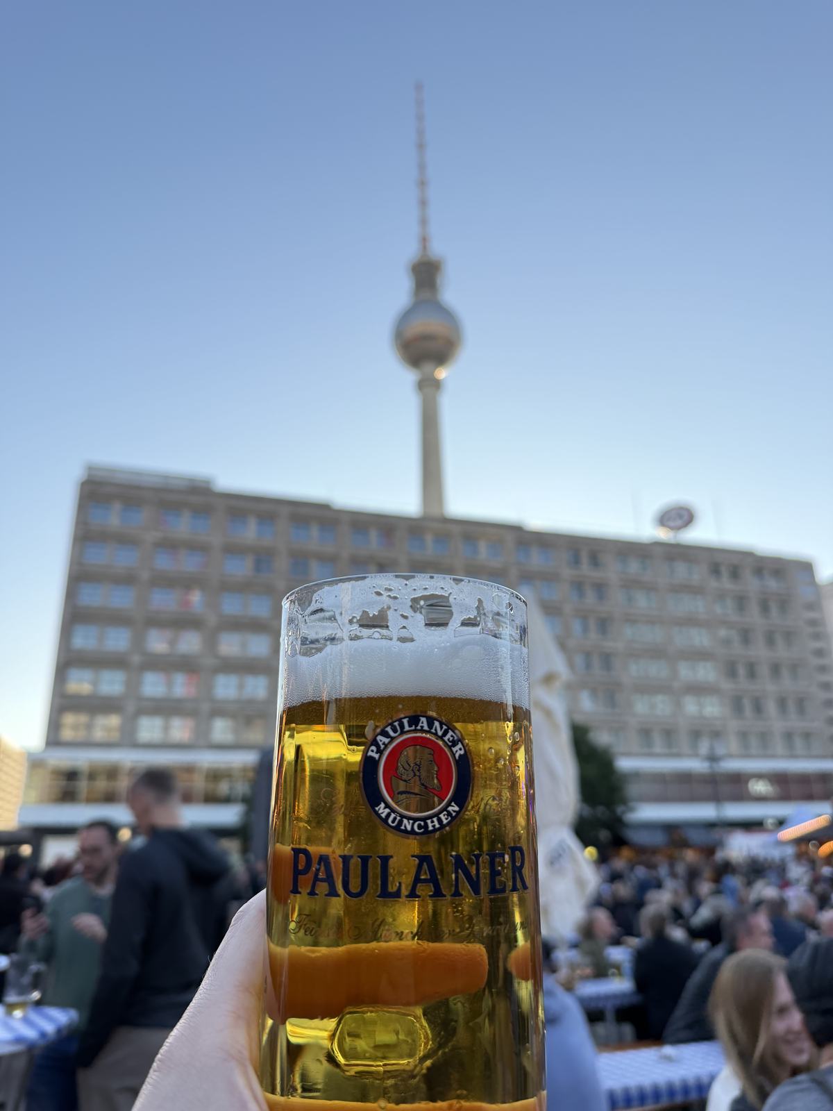 A Paulaner beer held up in front of the Berlin TV tower