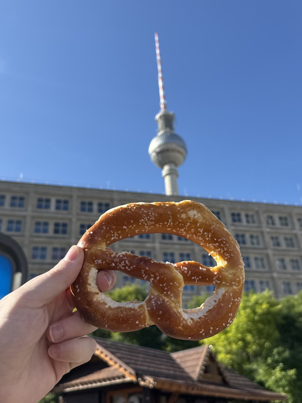 A large salted Brezel held up in front of the Berlin TV tower