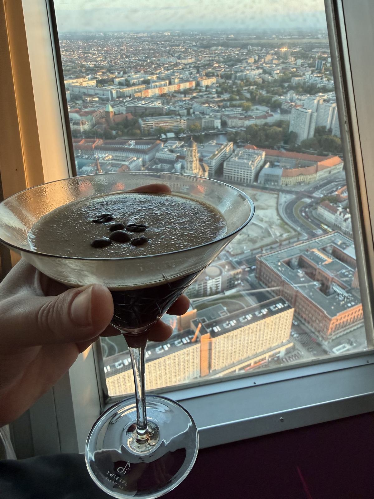 An espresso martini held up against the window of the TV tower