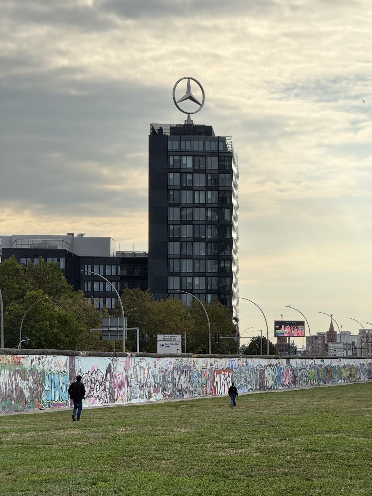 A bare stretch of the Berlin Wall in front of a Mercedes tower
