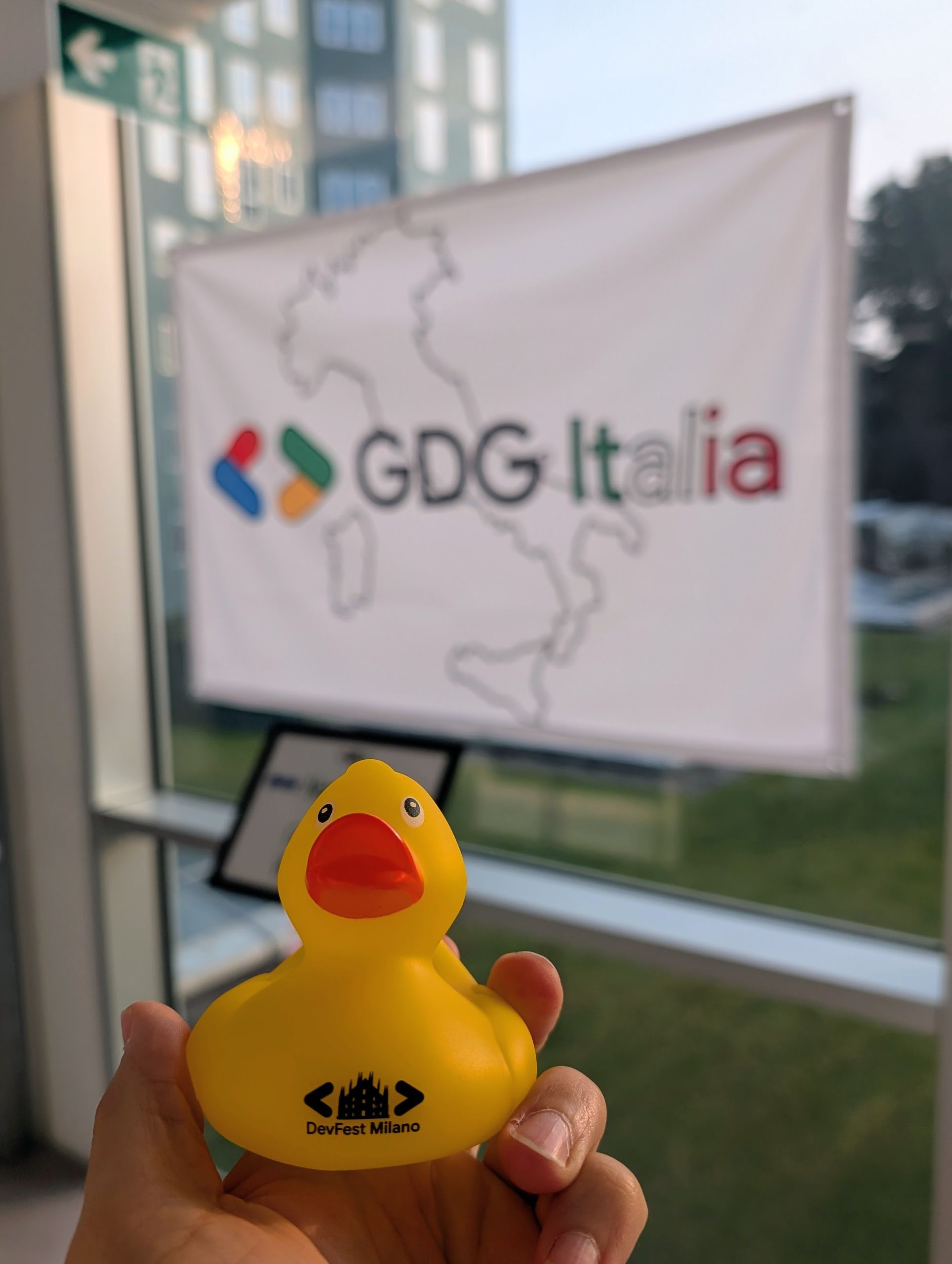 A yellow DevFest rubber duck held up in front of the GDG Italia banner