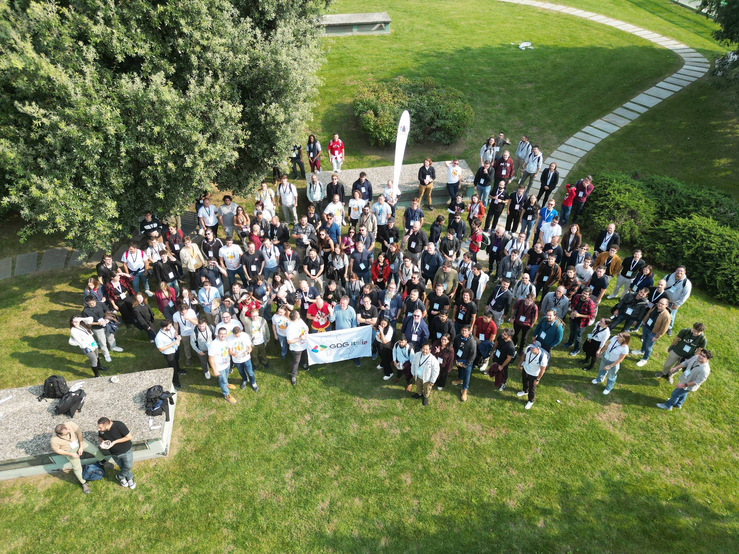 The group photo seen from the drone: about a hundred and fifty people on the grass around the GDG Italia banner