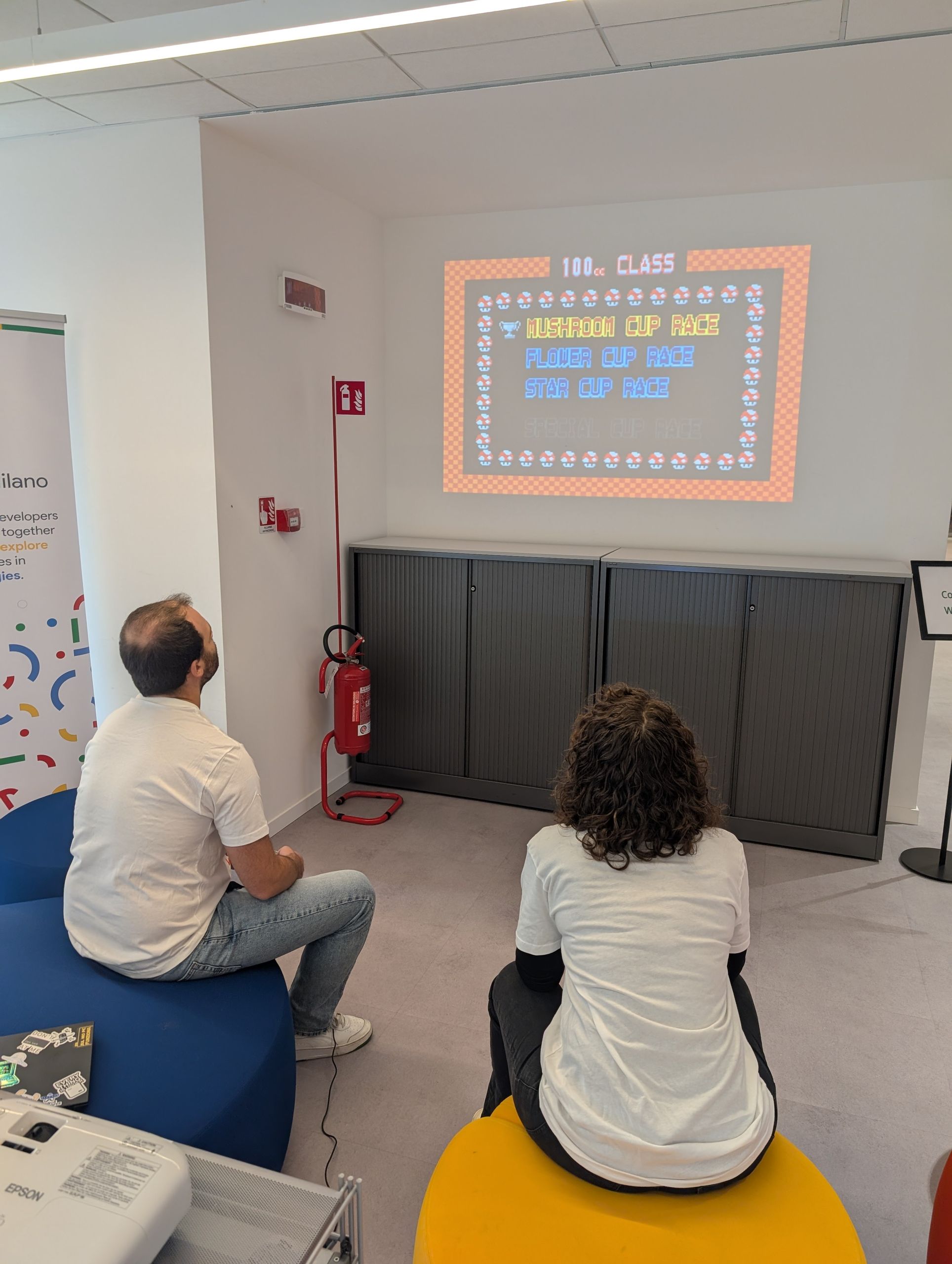 A small room with a pixel-art slide on the wall and people on poufs