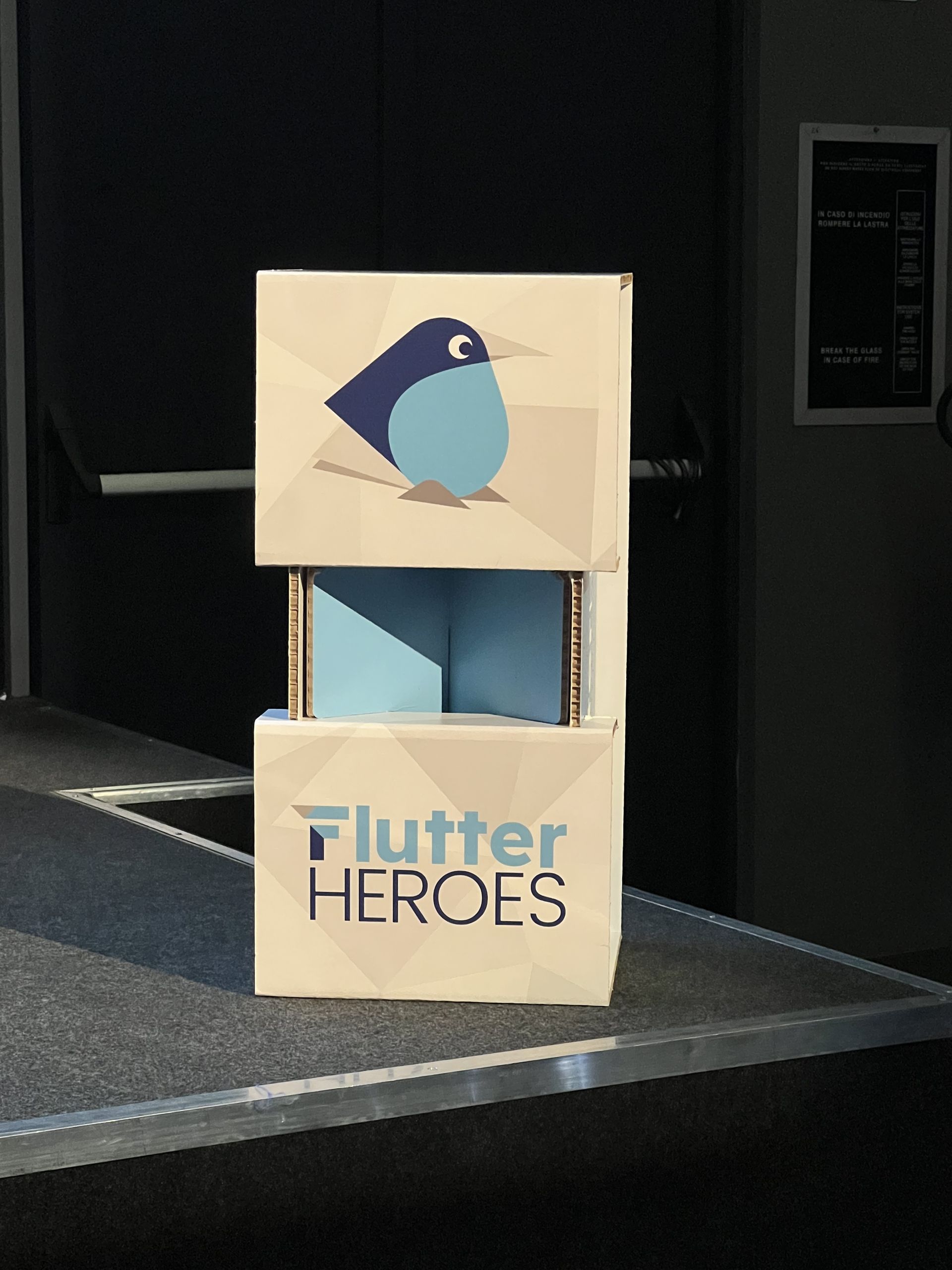 A cardboard stand printed with the Flutter Heroes bird next to the stairs