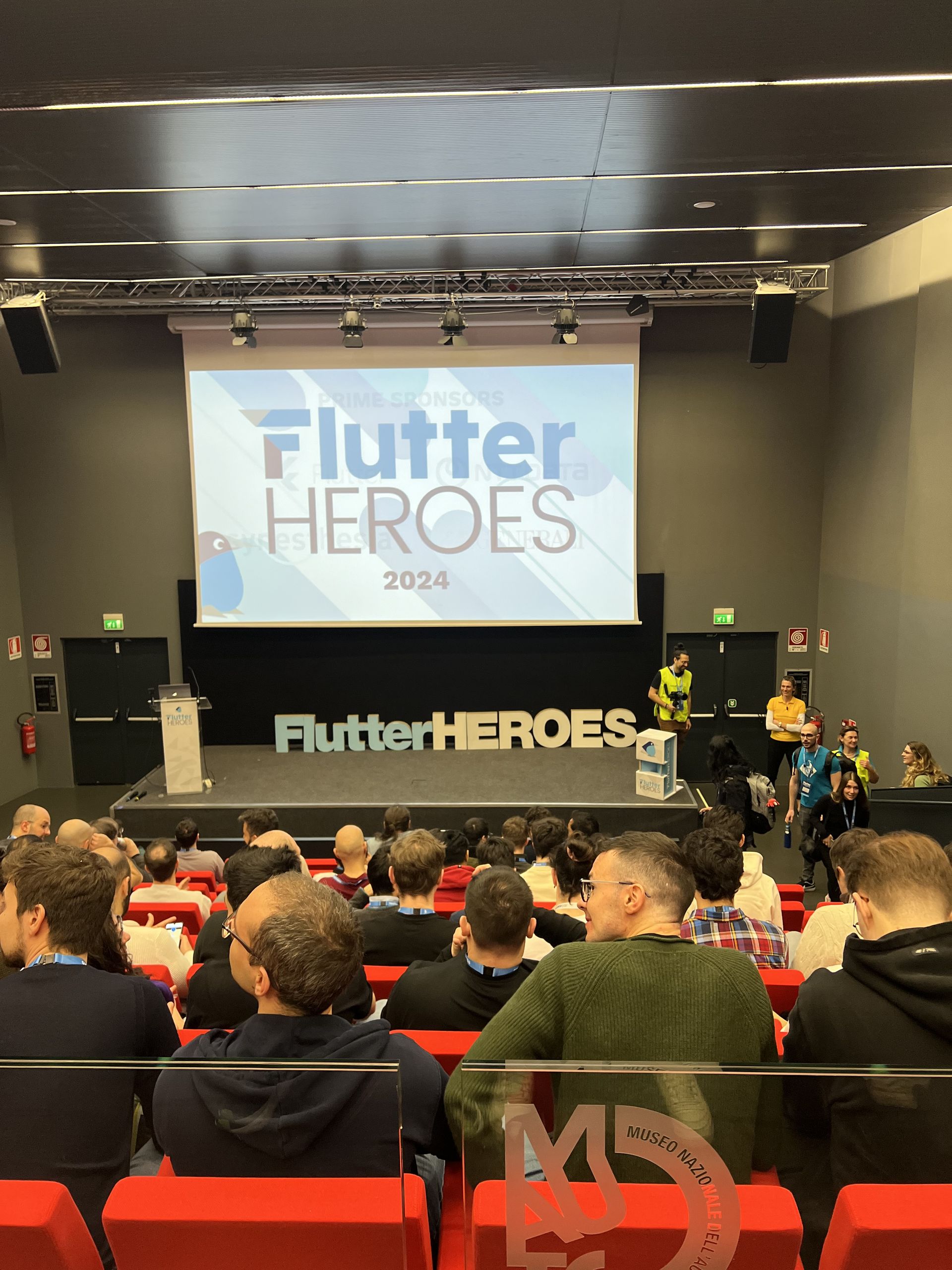 A speaker on stage in front of the Flutter Heroes screen