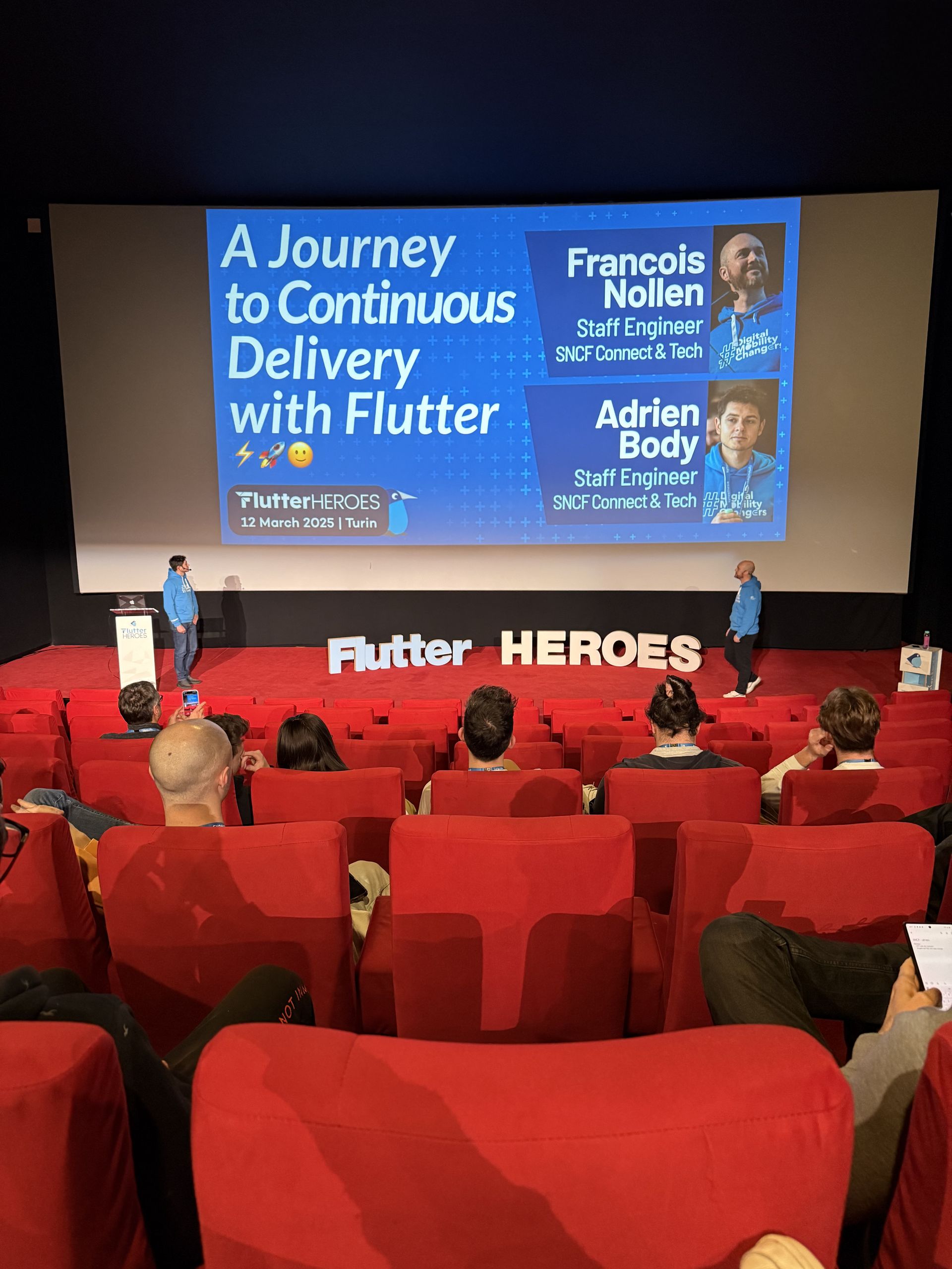 A Journey to Continuous Delivery with Flutter on the screen, with the two speakers on stage
