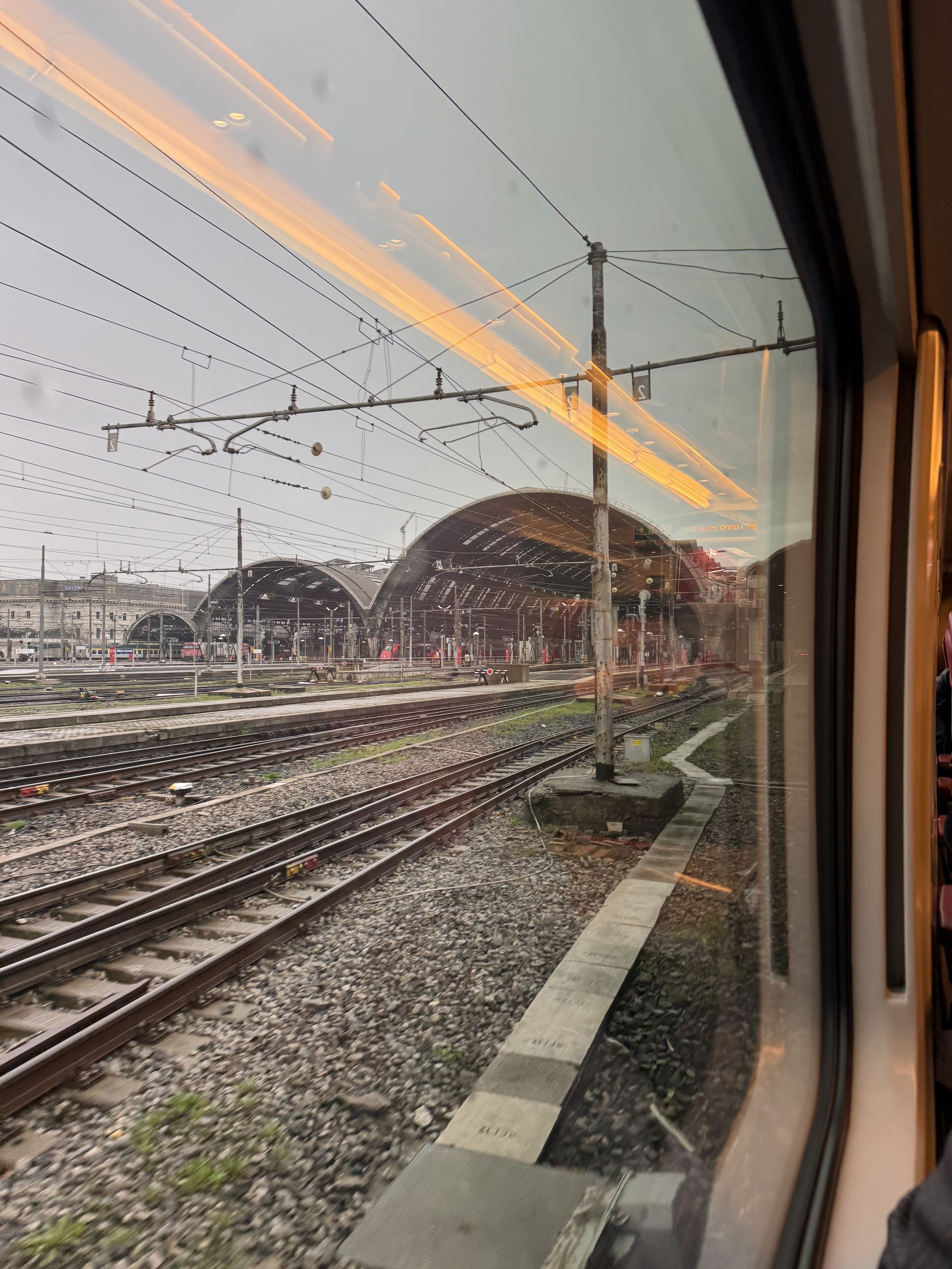 Railway tracks and a station train shed seen from a train window early in the morning