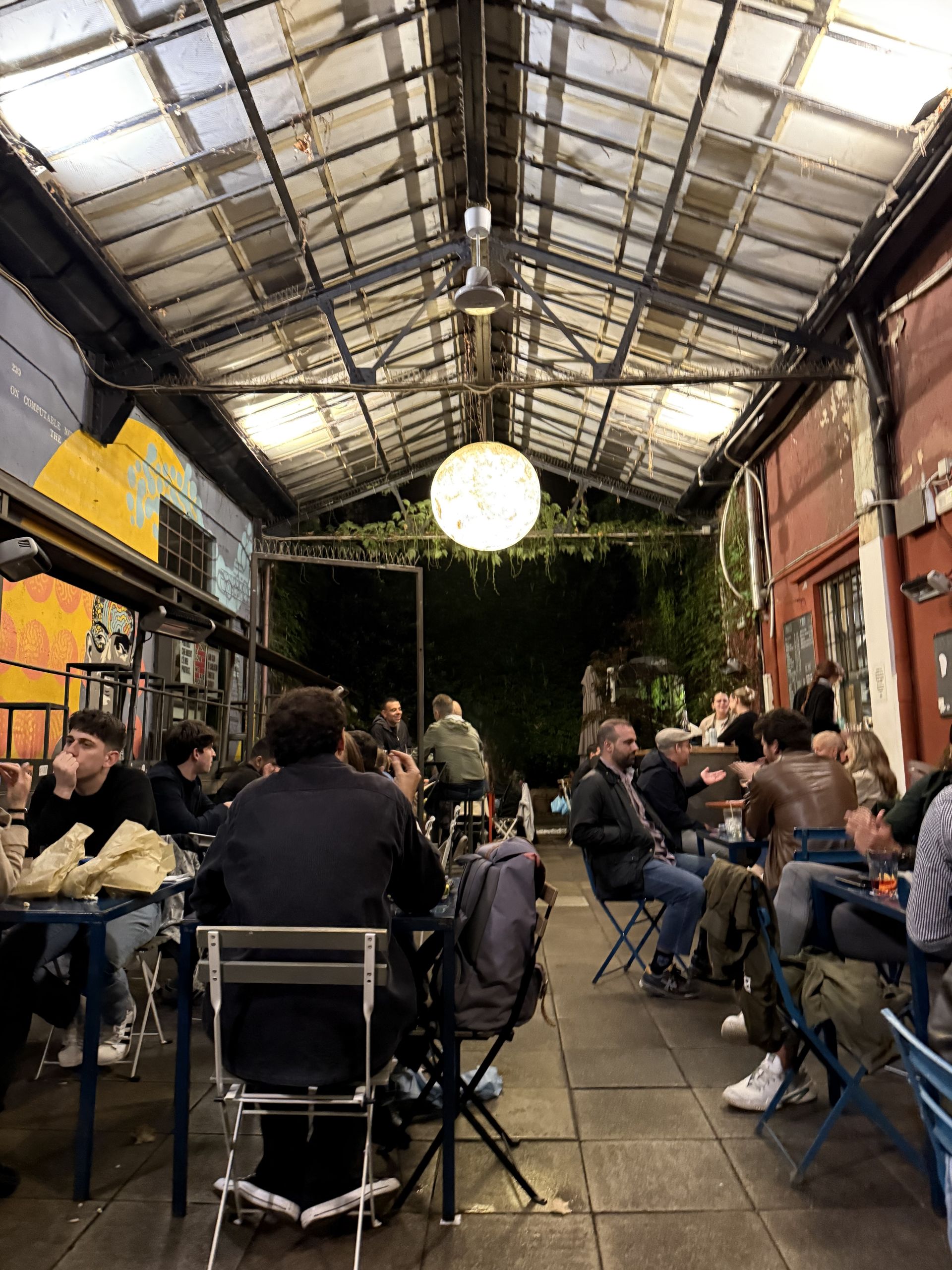 A busy restaurant under a glass roof late in the evening