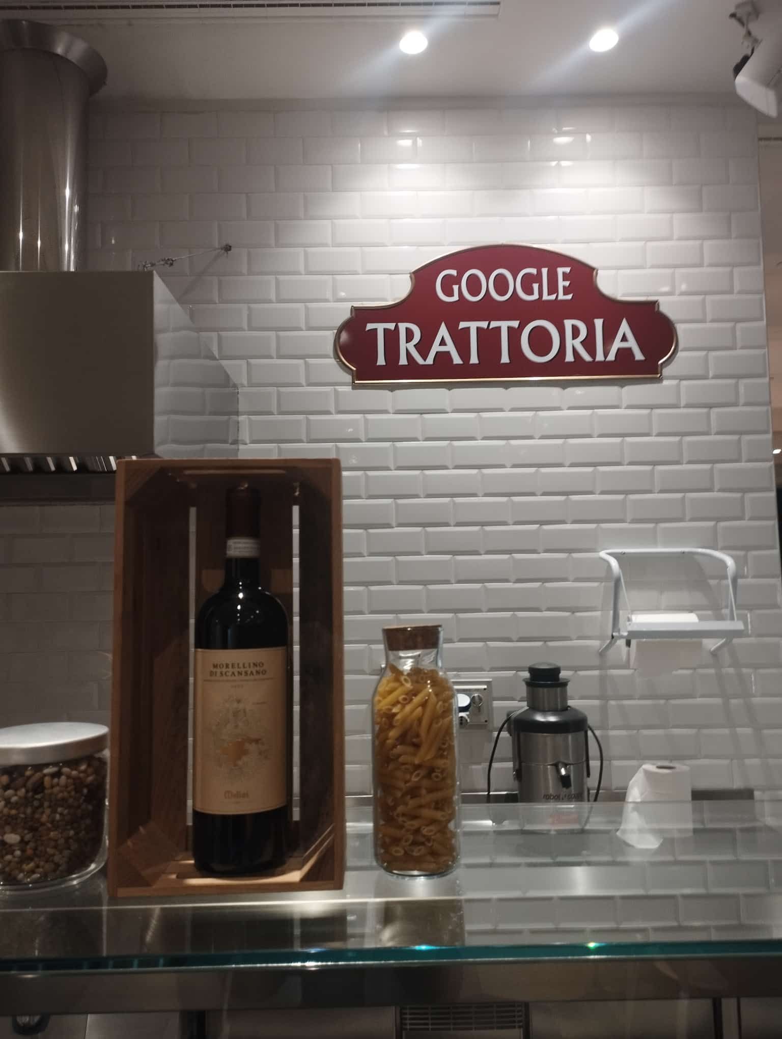 A brown enamel sign reading GOOGLE TRATTORIA on the white tiled wall of the canteen