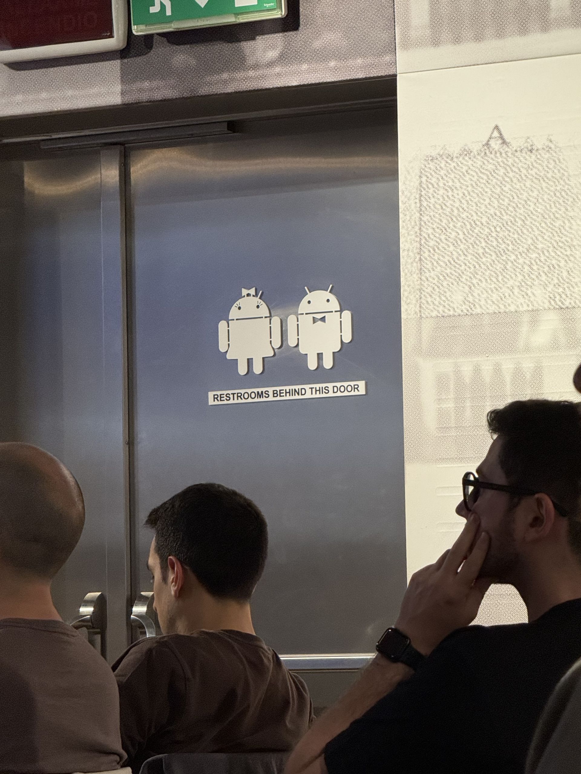 A door signposted Washrooms behind this door with two Android robots on it