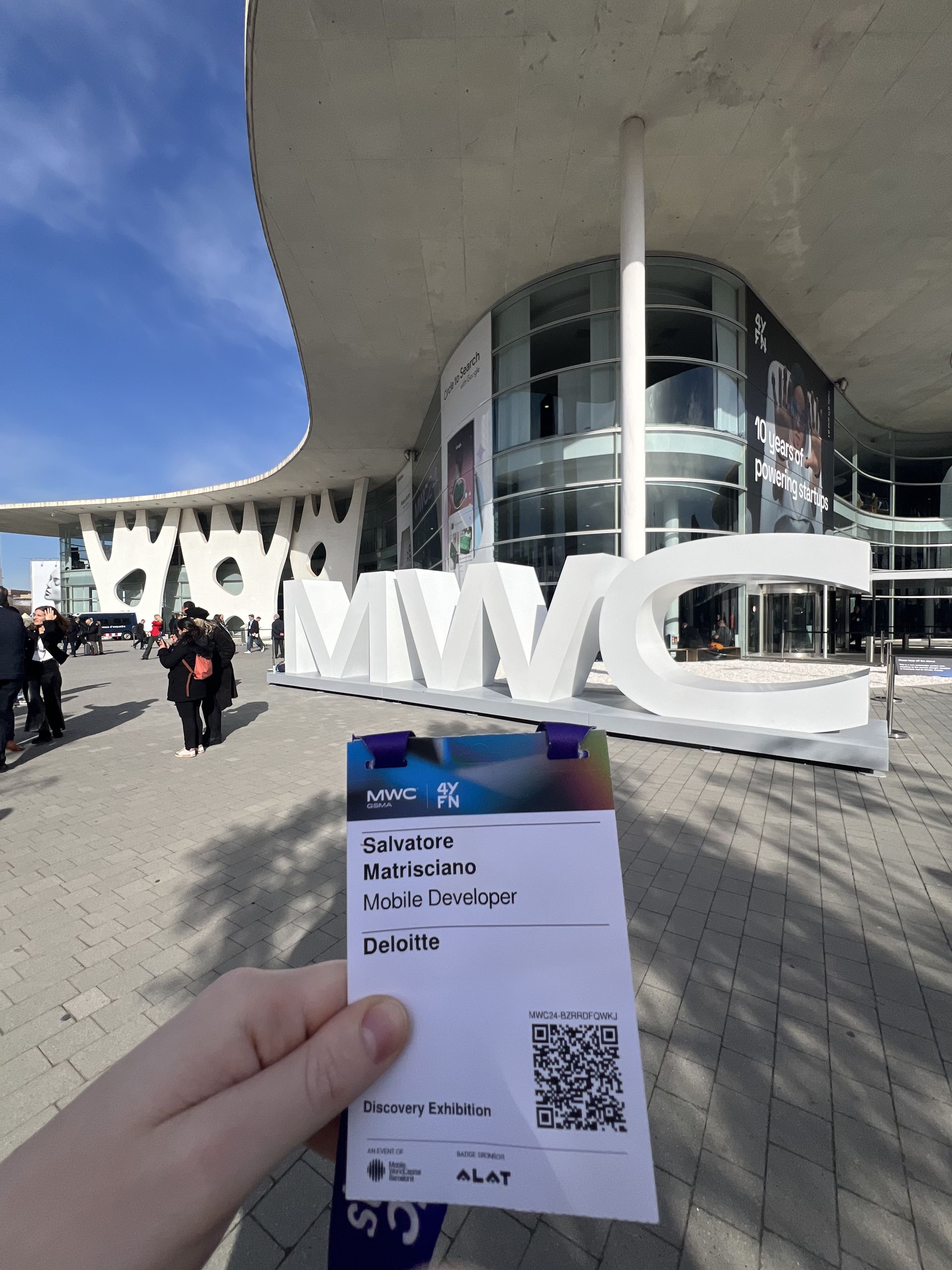 The badge held up in front of the MWC letters outside the venue
