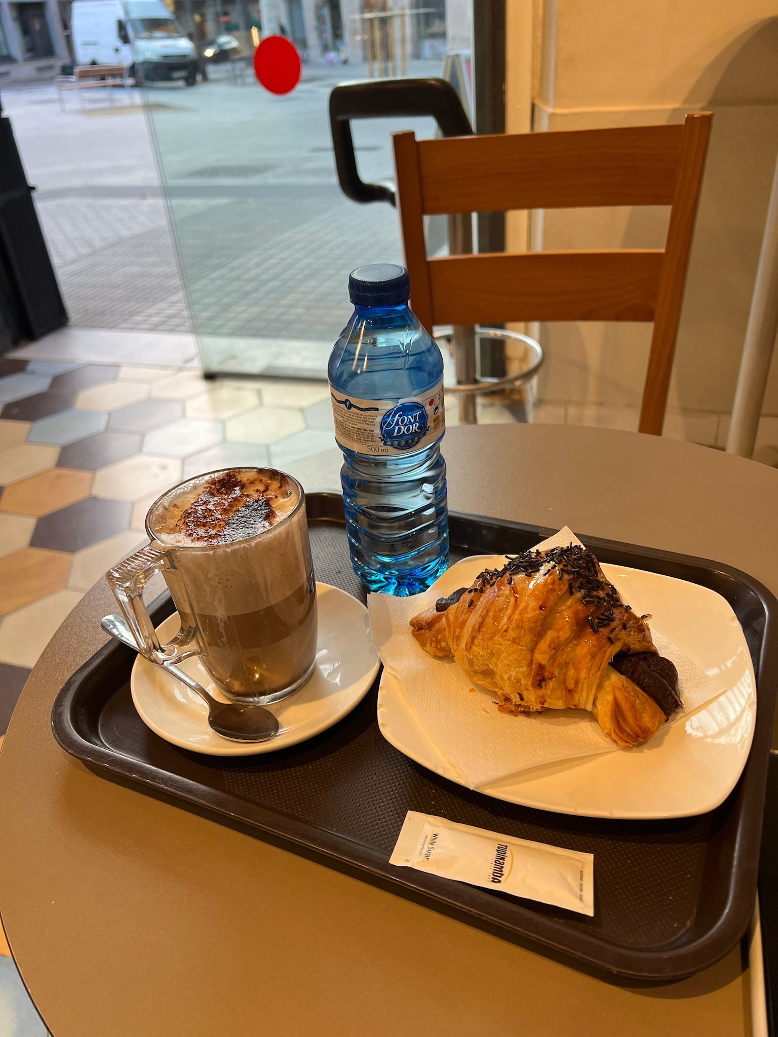 Cortado and a chocolate croissant on a tray at a bar