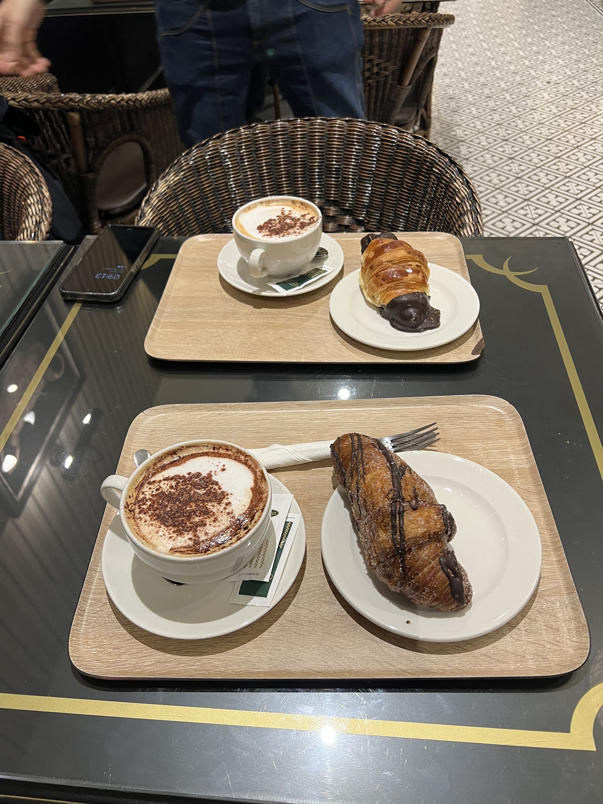 Two breakfast trays with cappuccinos and chocolate croissants