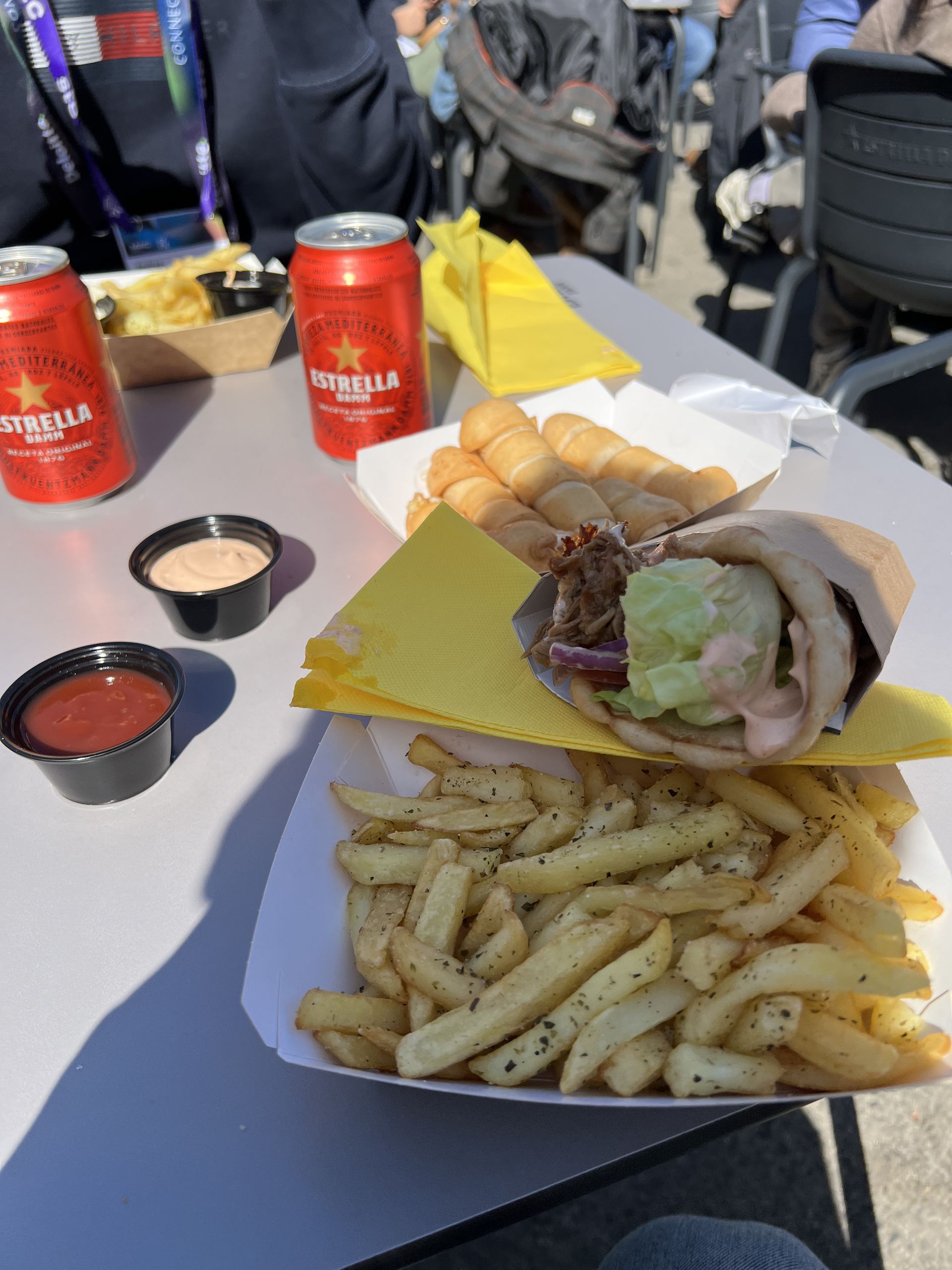A wrap and chips with Estrella Damm cans at an outdoor table at the Fira